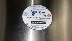 Facilitec Southwest NFPA 96 Certificate of Performance service label attached to a stainless steel commercial kitchen hood after cleaning