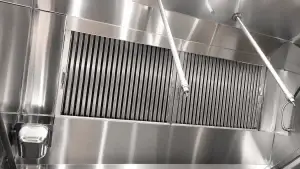 Clean stainless steel commercial kitchen exhaust hood with polished baffle filters, metal panels, and overhead fire suppression nozzles