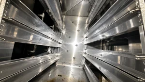 Clean stainless steel interior of a commercial kitchen exhaust duct system with access rails, metal panels, and drainage area visible.